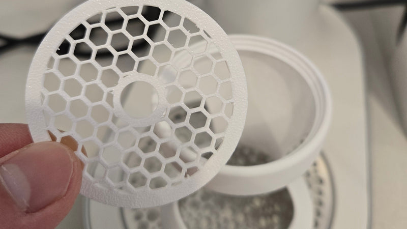 Close-up of a white honeycomb filter held in front of a white appliance.