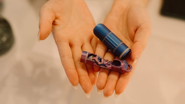 Two hands holding two small, colorful objects against a neutral background